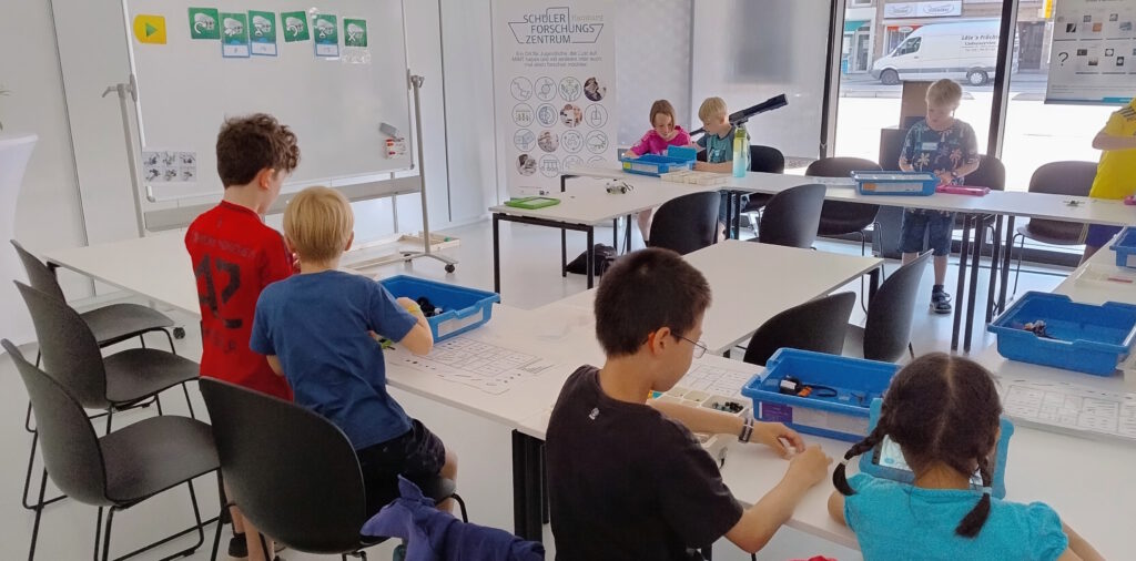 Kinder sitzen an Tischen und bauer aus Lego-Steinen ein Robotermodell.